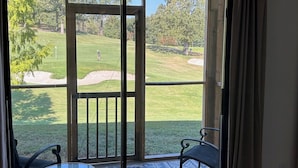 A room with a sliding glass door leading to a balcony with a view of a golf course.