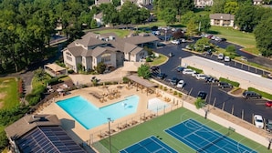 An aerial view of a residential area with a swimming pool, tennis courts, and a solar panel building.