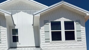 Una casa de dos pisos con garaje, una puerta principal y dos ventanas con persianas.