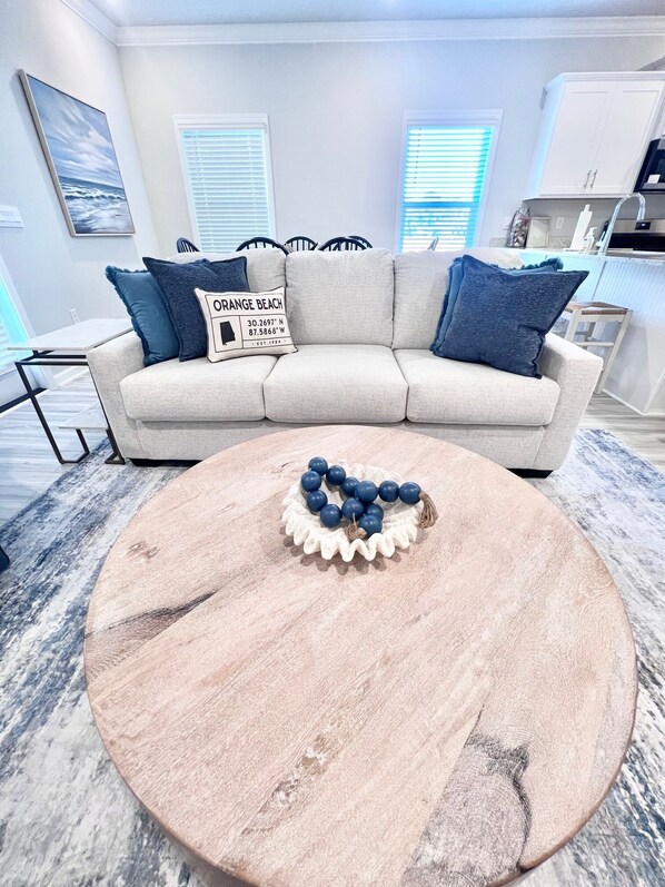A living room with a beige sofa, a round coffee table with a blue and white centerpiece, and a painting on the wall. - Modern 3 Bedroom Retreat! 5 minutes to the beach, 3 minutes to the Wharf (Orange Beach)