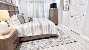 Une chambre à coucher comprenant un lit, une table de chevet, une commode, un téléviseur et une porte.