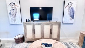 Un salon avec une table basse ronde en bois, un téléviseur à écran plat, des meubles en bois et deux tableaux représentant un héron, accrochés au mur.