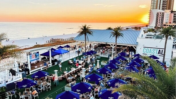 Un restaurant situé sur la côte, avec une terrasse et une vue sur la plage au coucher du soleil.