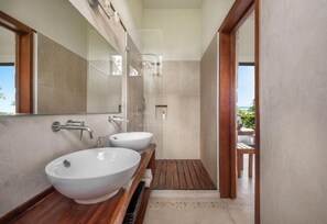 A modern bathroom with two large white sinks, a glass shower enclosure, and a wooden vanity.