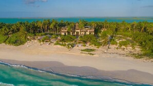 Una propiedad frente a la playa con un edificio grande rodeado de palmeras y una playa arenosa.