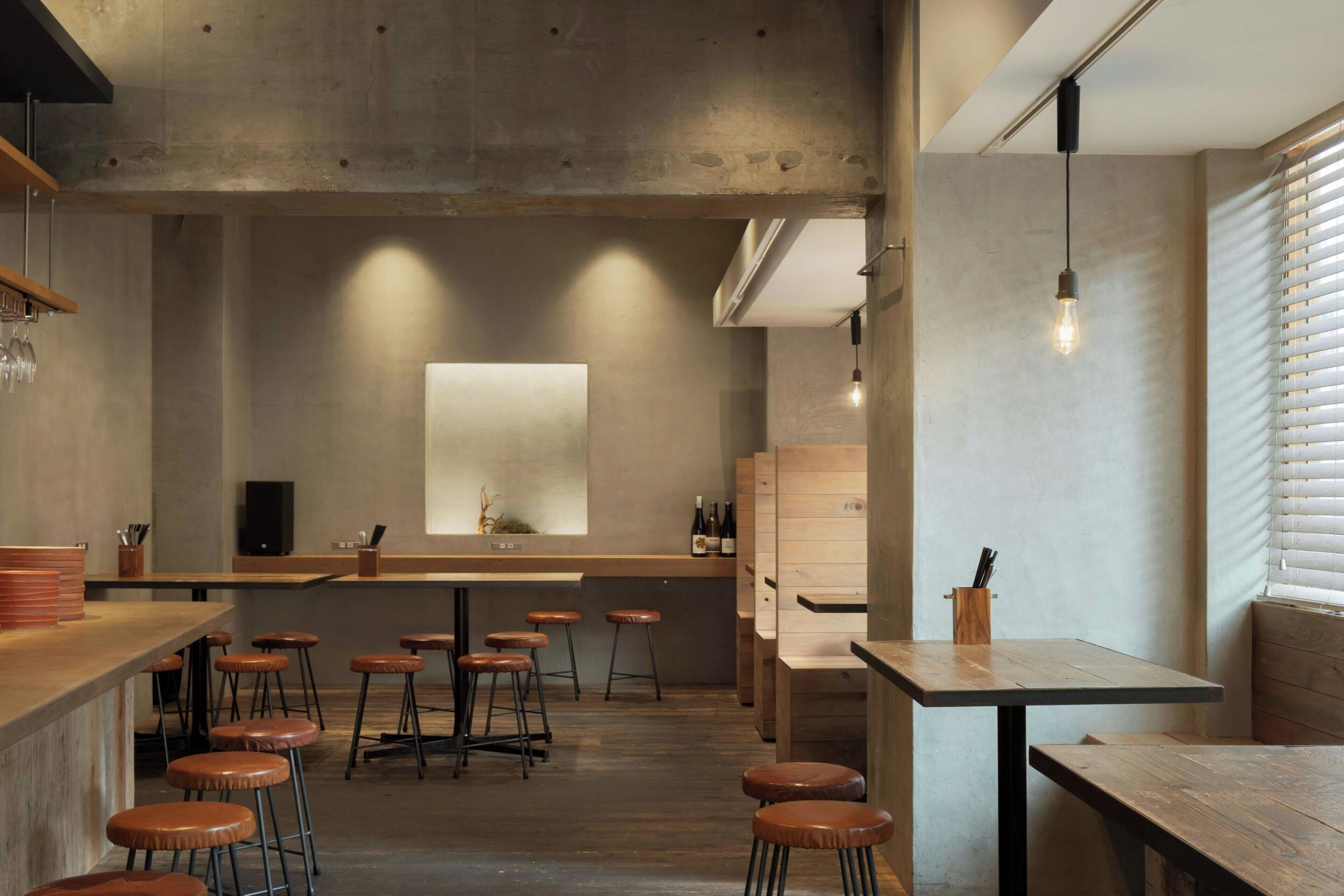 Zona de bar moderna con taburetes, mostrador y un ventanal con persianas.