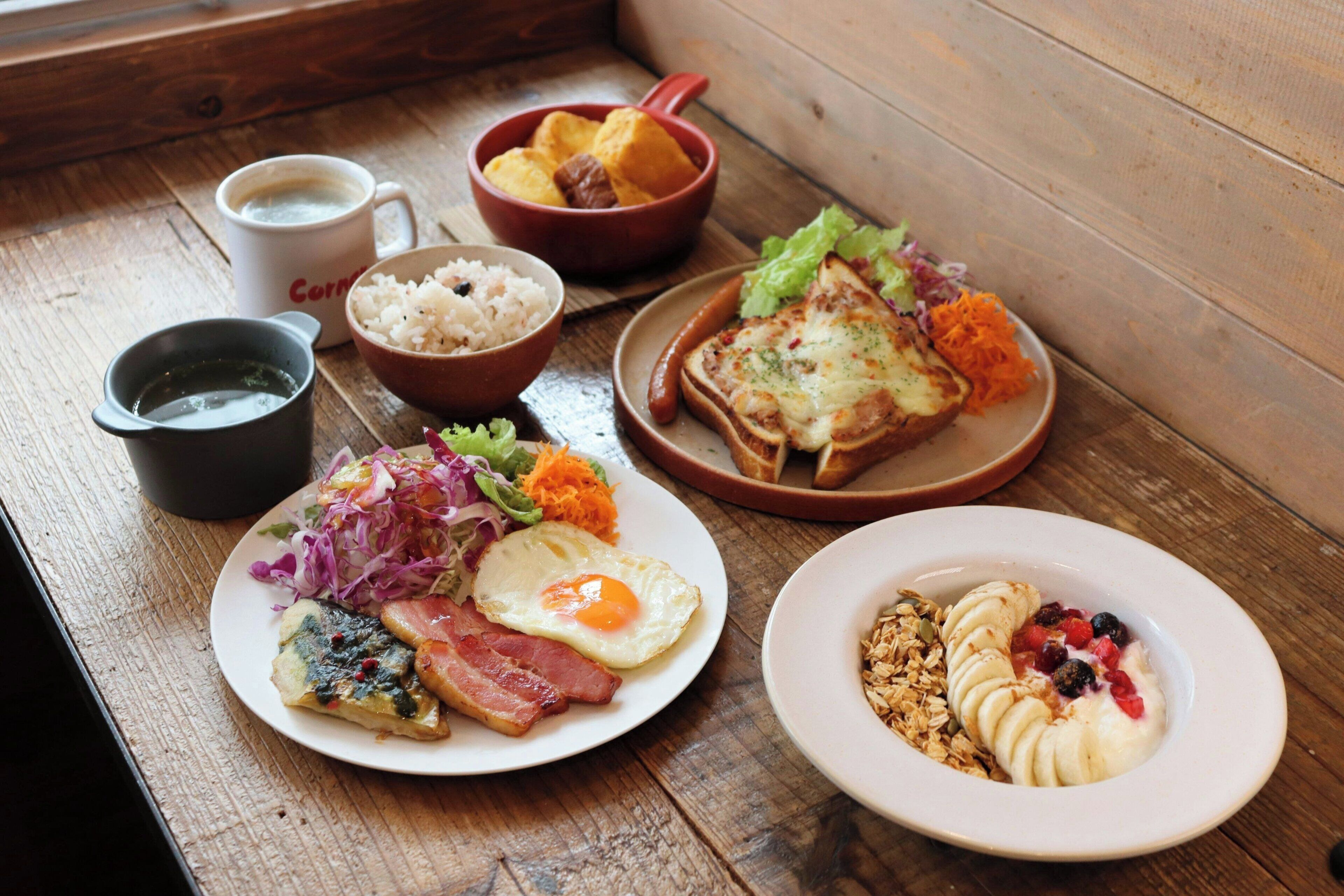 A wooden table with various breakfast items including eggs, bacon, toast, rice, and a bowl of fruit.