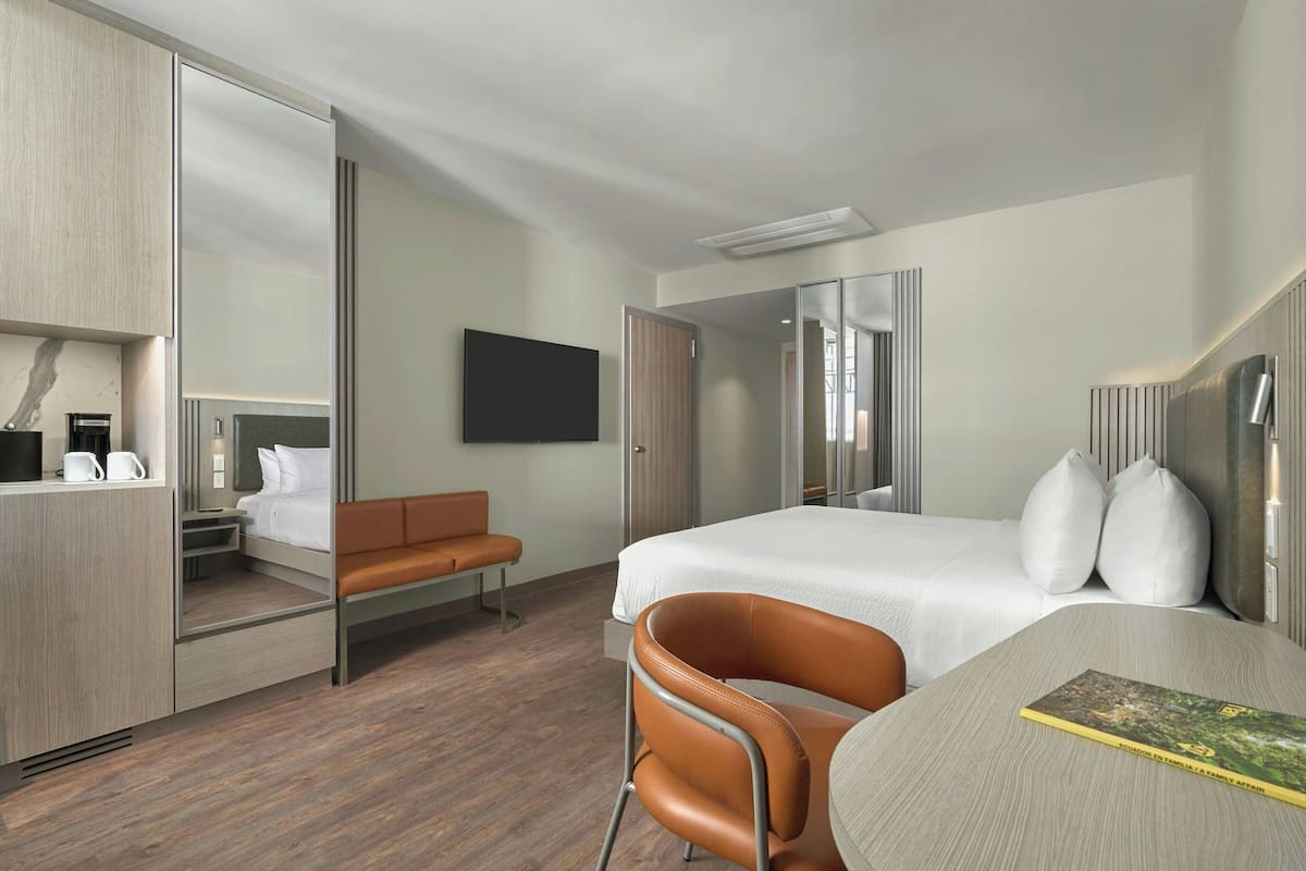 Una habitación de hotel moderna con cama, escritorio, silla, televisor y armario.