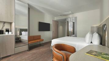 Una habitación de hotel moderna con cama, escritorio, silla, televisor y armario.