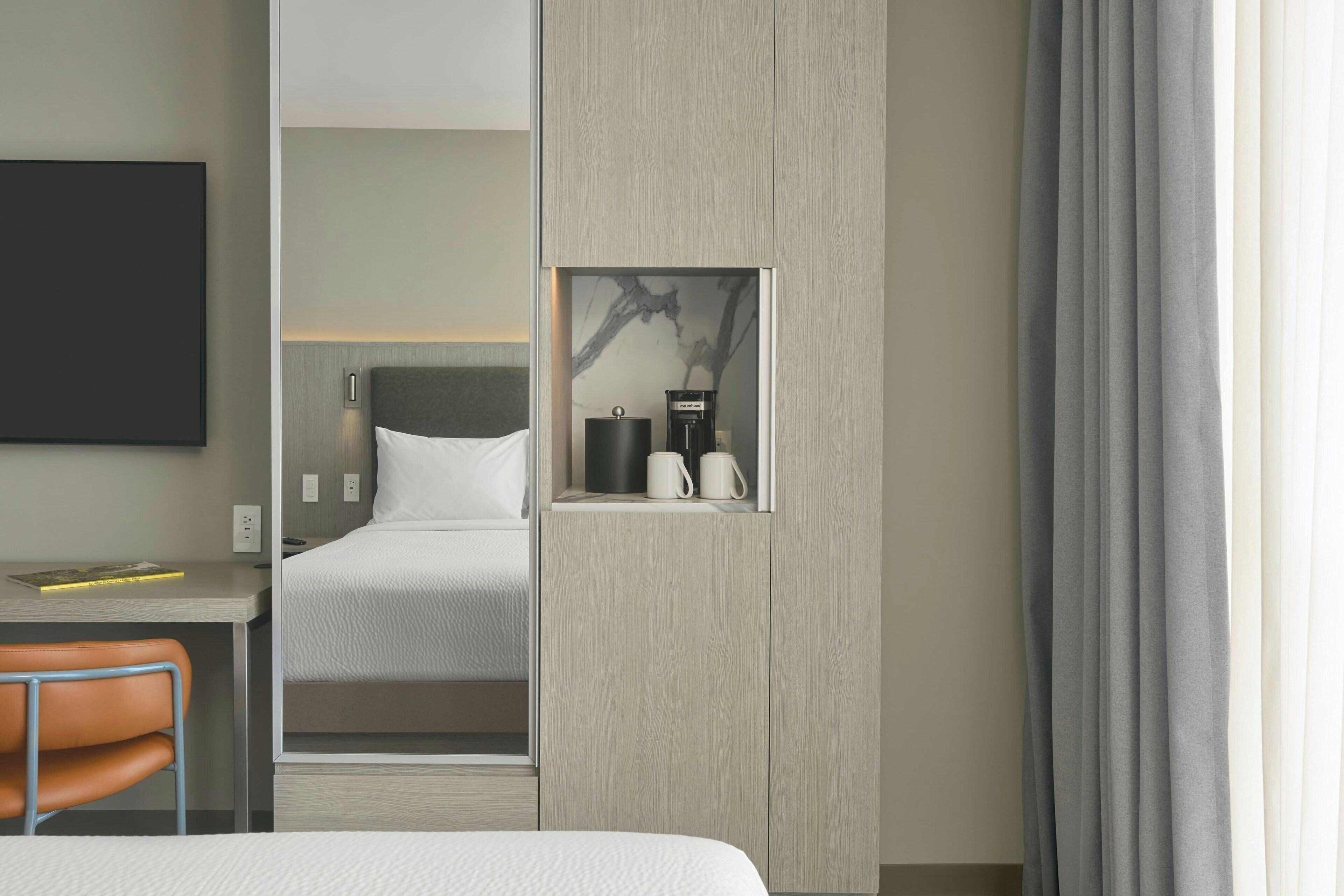 Een hotelkamer met een bed, een bureau, een stoel, een koffiezetapparaat en een aan de muur bevestigde televisie.