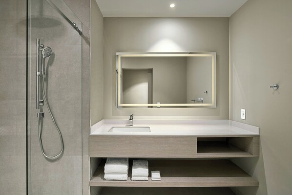 Un baño moderno con cabina de ducha de vidrio, un lavamanos blanco y un espejo encima.