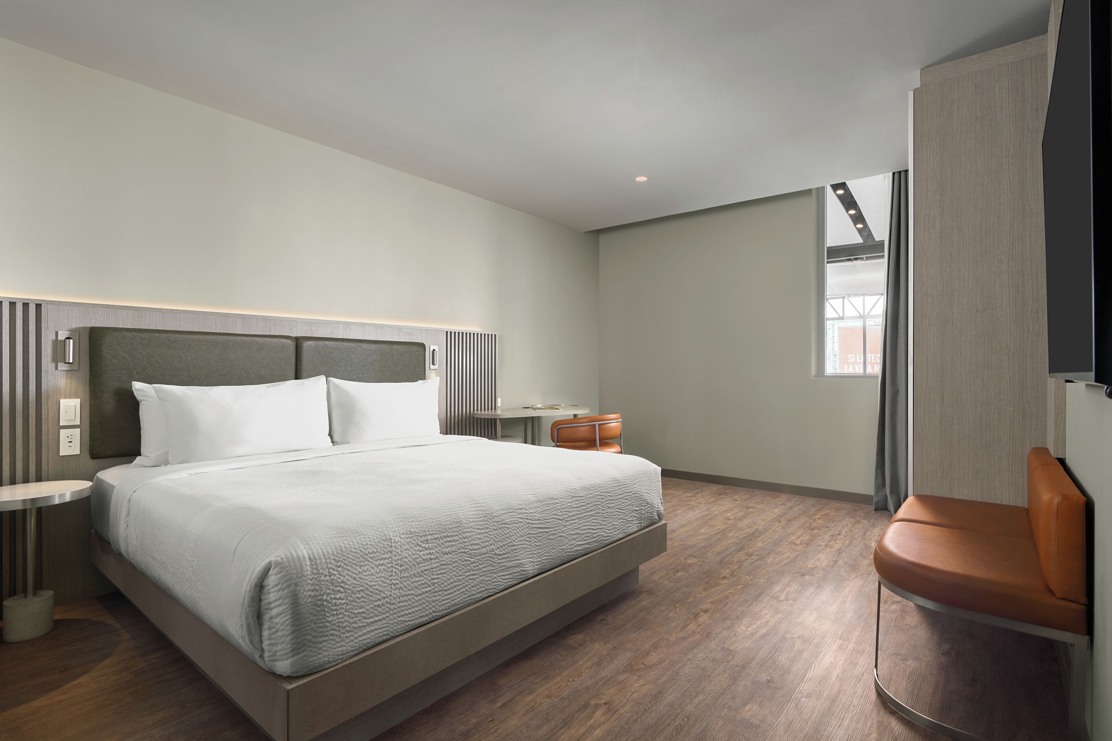 A modern hotel room with a large bed, bedside tables, a chair, and a TV.