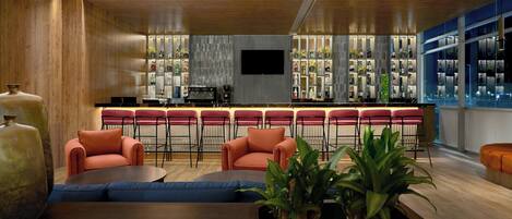 Zona de bar con asientos, un televisor y estantes con botellas.