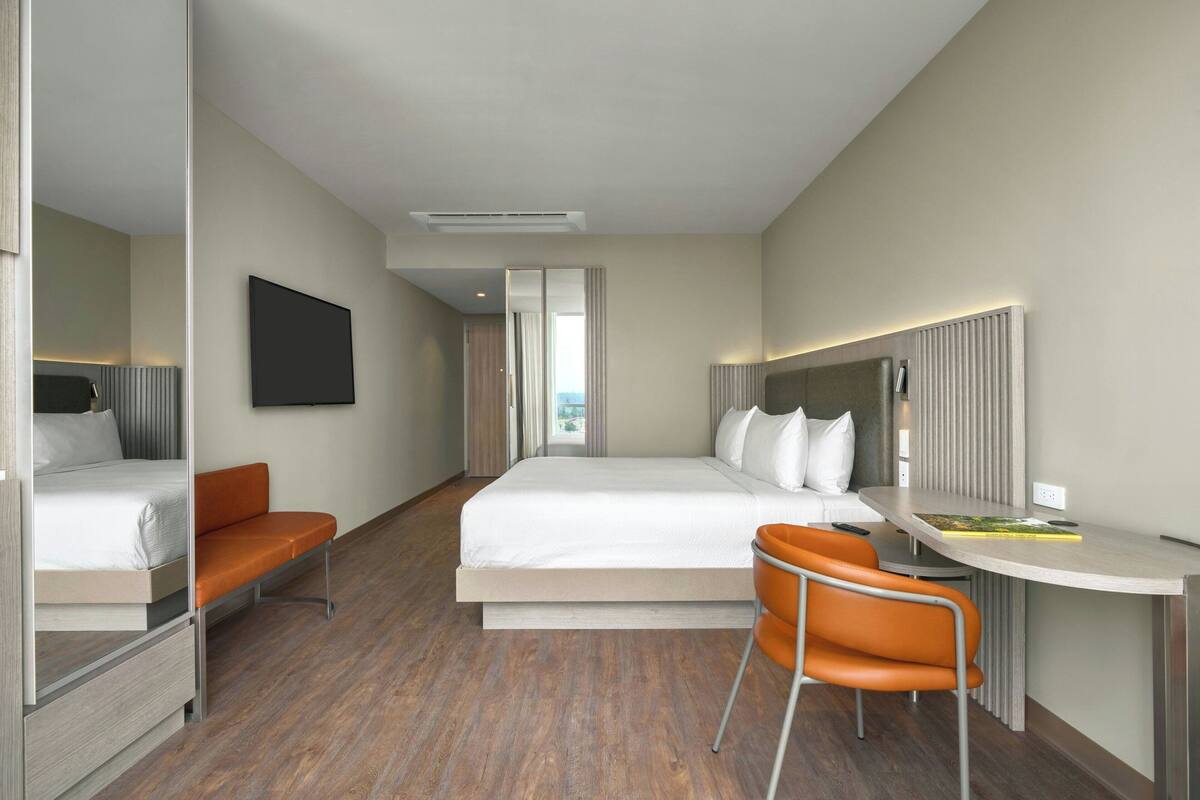 Una habitación de hotel moderna con una cama, un escritorio, una silla y un ventanal grande.