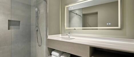 Un baño moderno con ducha de vidrio, un espejo grande y tocador con lavamanos y espacio para toallas.