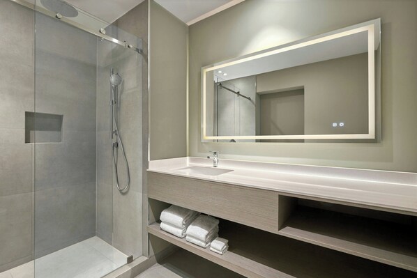 A modern bathroom with a glass-enclosed shower, a large mirror, and a vanity with a sink and towel storage. - Courtyard By Marriott Quito Airport (Tababela)