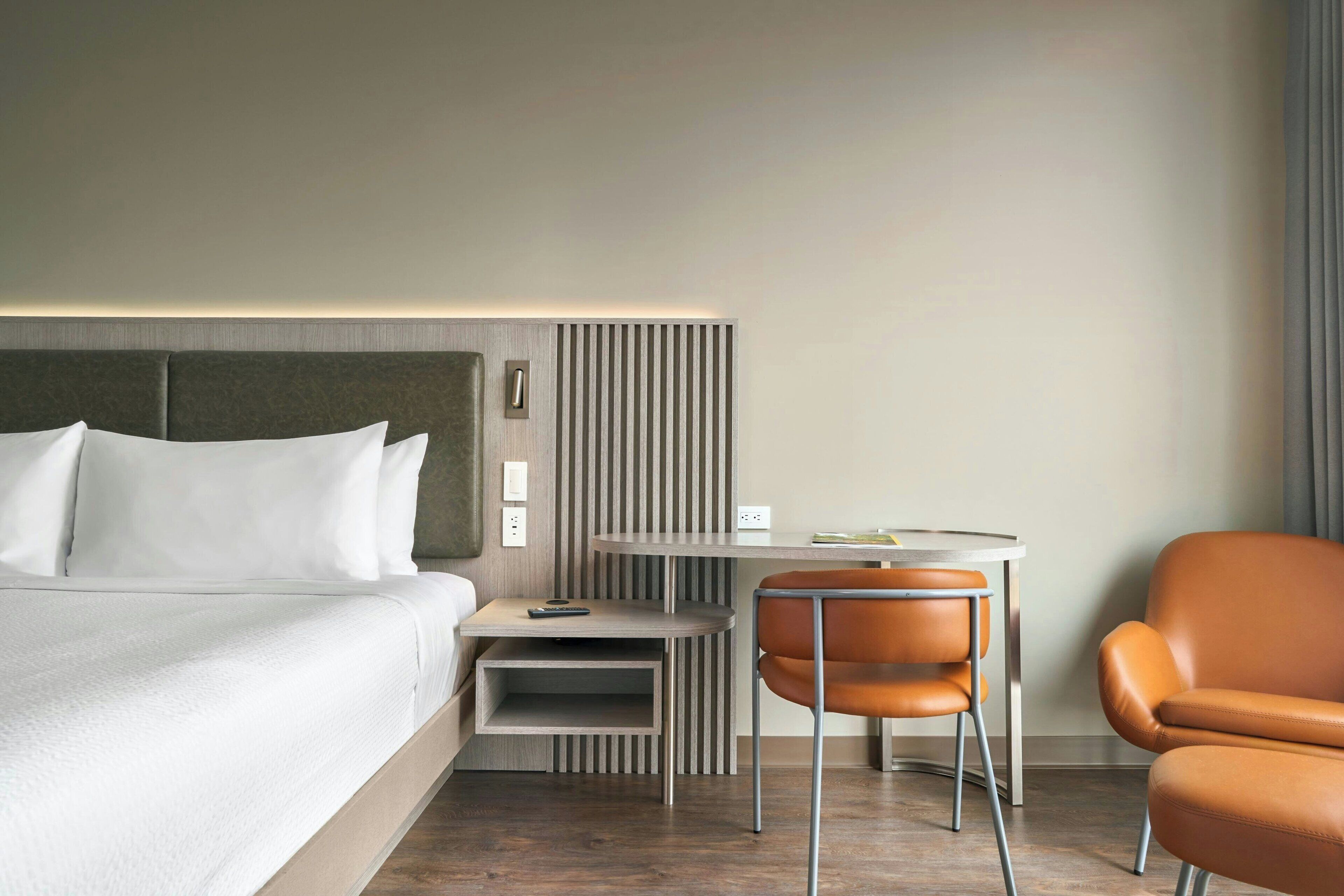 Een moderne hotelkamer met een bed, een klein tafeltje, een stoel en een paneel aan de muur.