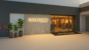 Entrada de un hotel Courtyard by Marriott con diseño moderno, plantas en macetas y un interior bien iluminado visible a través de puertas de vidrio.