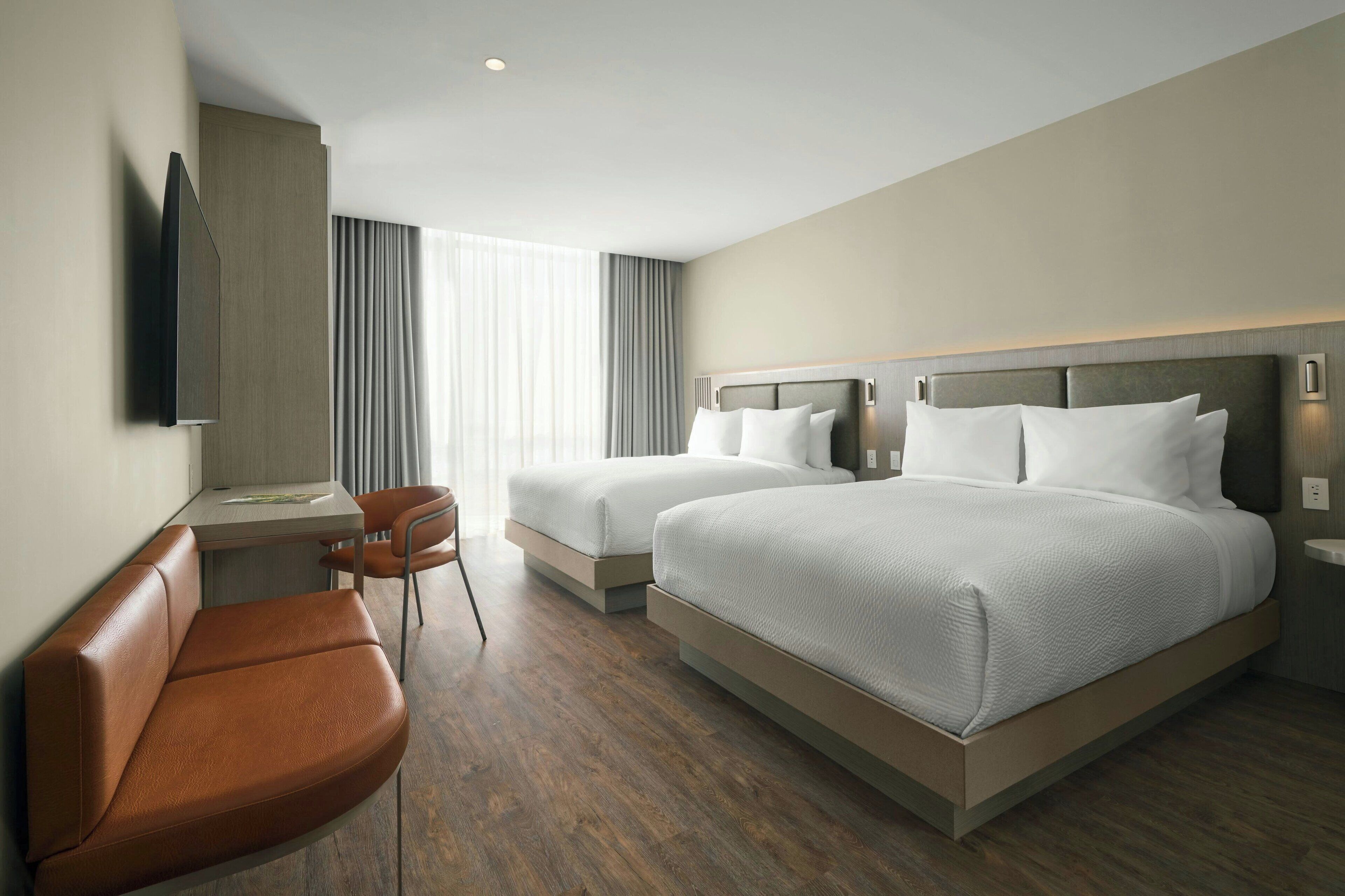 A hotel room with two beds, a desk, a chair, and a TV mounted on the wall.