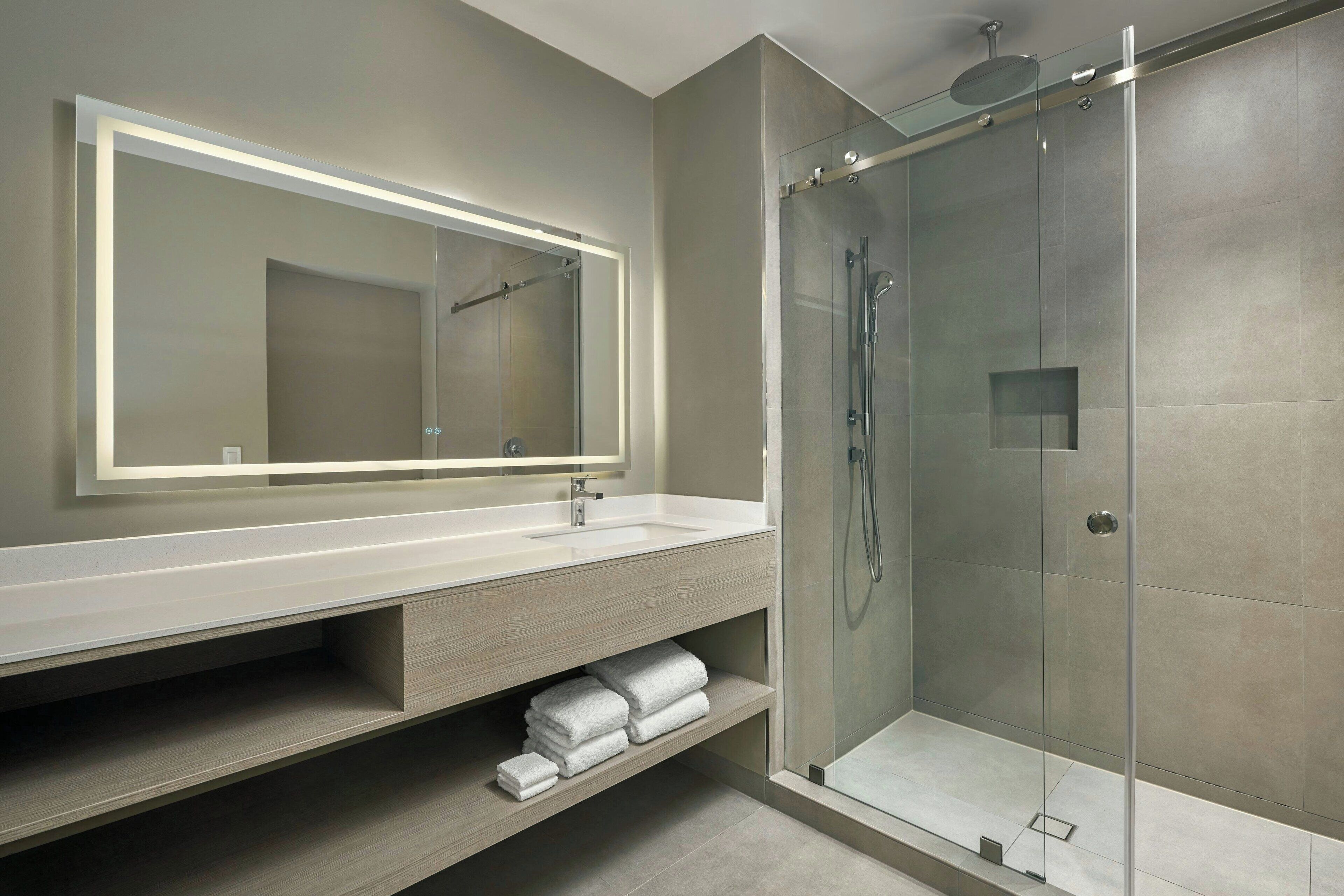 Une salle de bain moderne dotée d’un grand miroir, d’une cabine de douche et d’un meuble-lavabo avec un espace pour ranger les serviettes.
