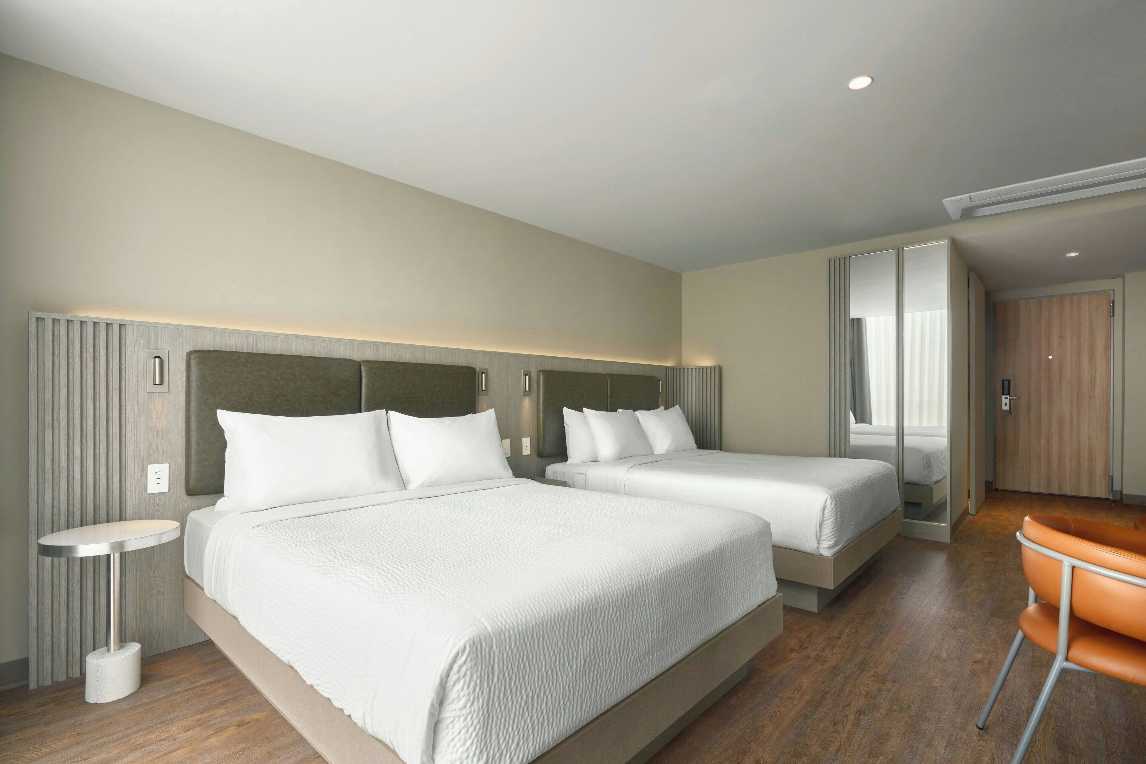 A hotel room with two beds, a small round table, a chair, and a wardrobe.
