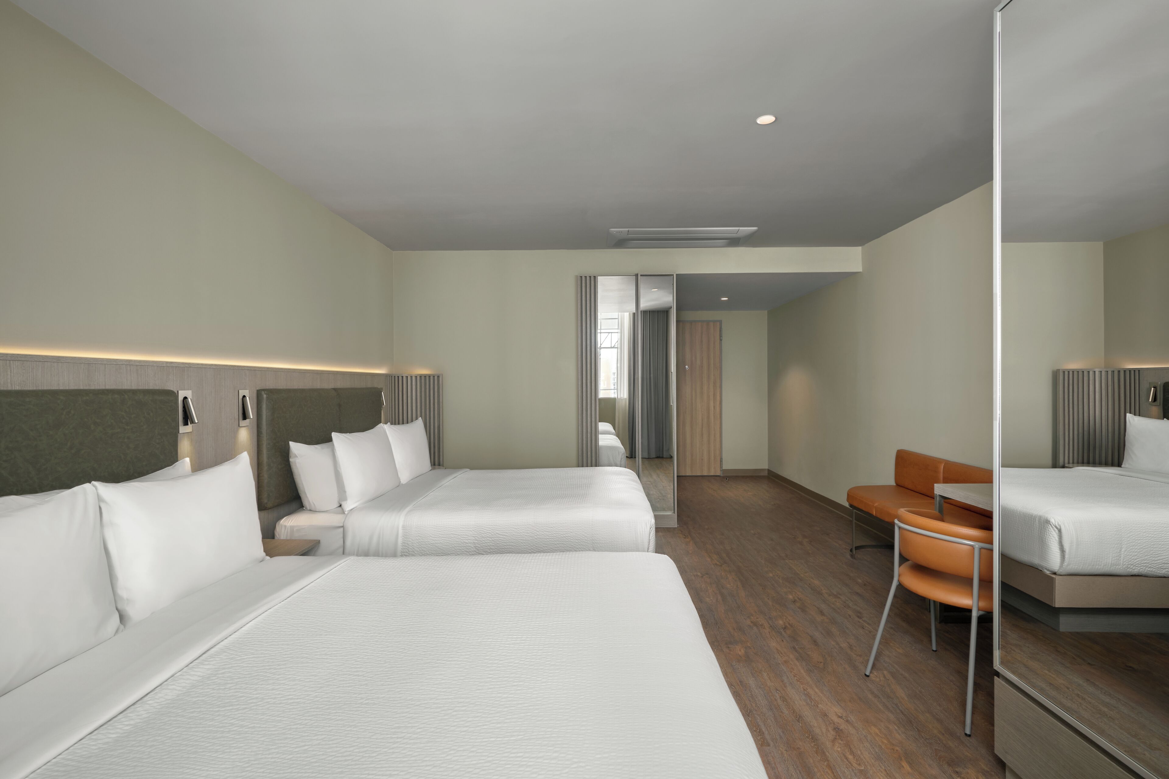 Ein Hotelzimmer mit zwei Betten, Holzboden, einem Spiegel und einer kleinen Sitzecke.