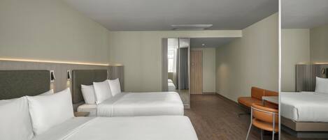 Habitación de hotel con dos camas, piso de madera, un espejo y un pequeño rincón de descanso.