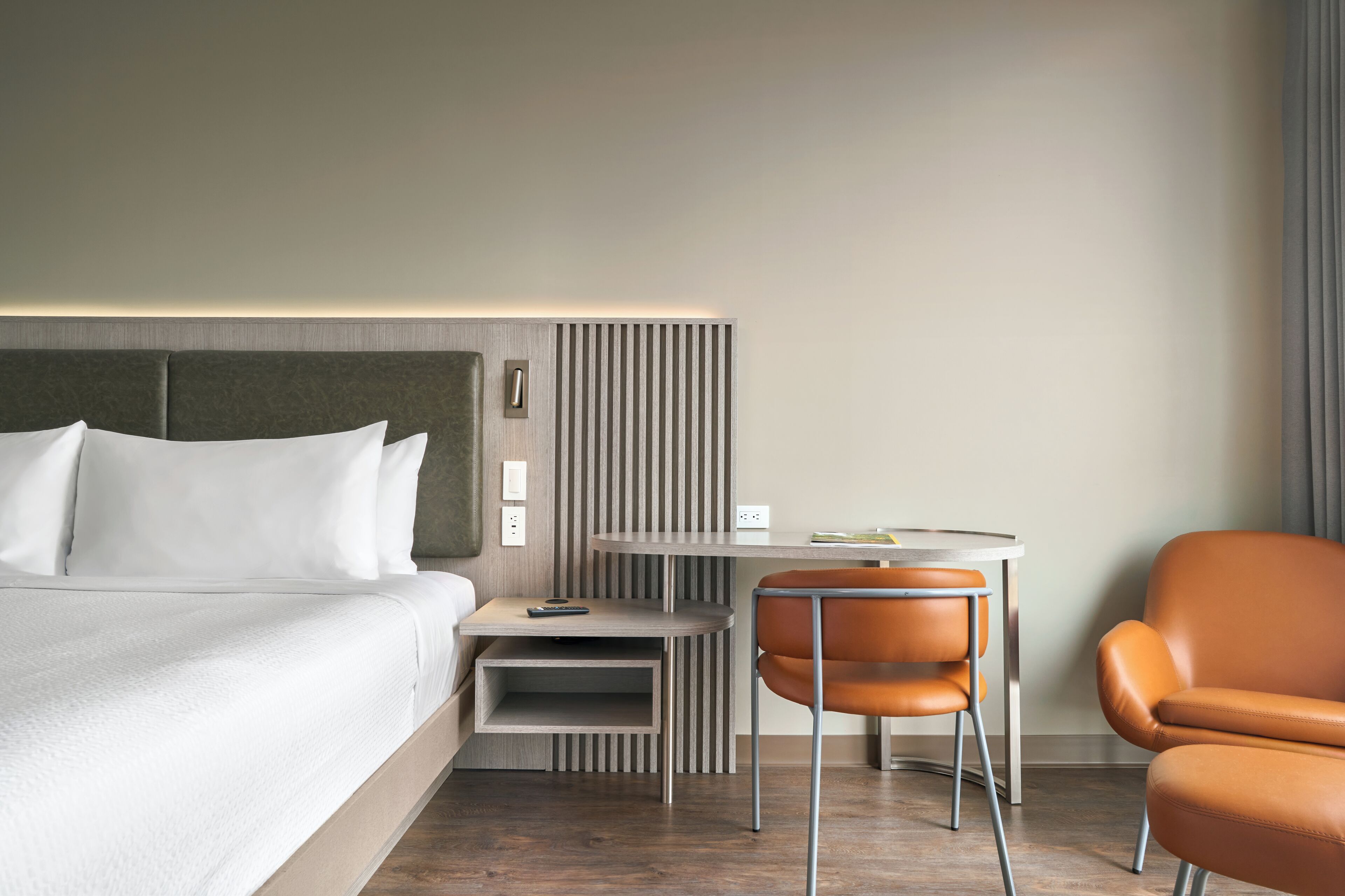 A modern hotel room with a bed, a small desk, a chair, and a nightstand.
