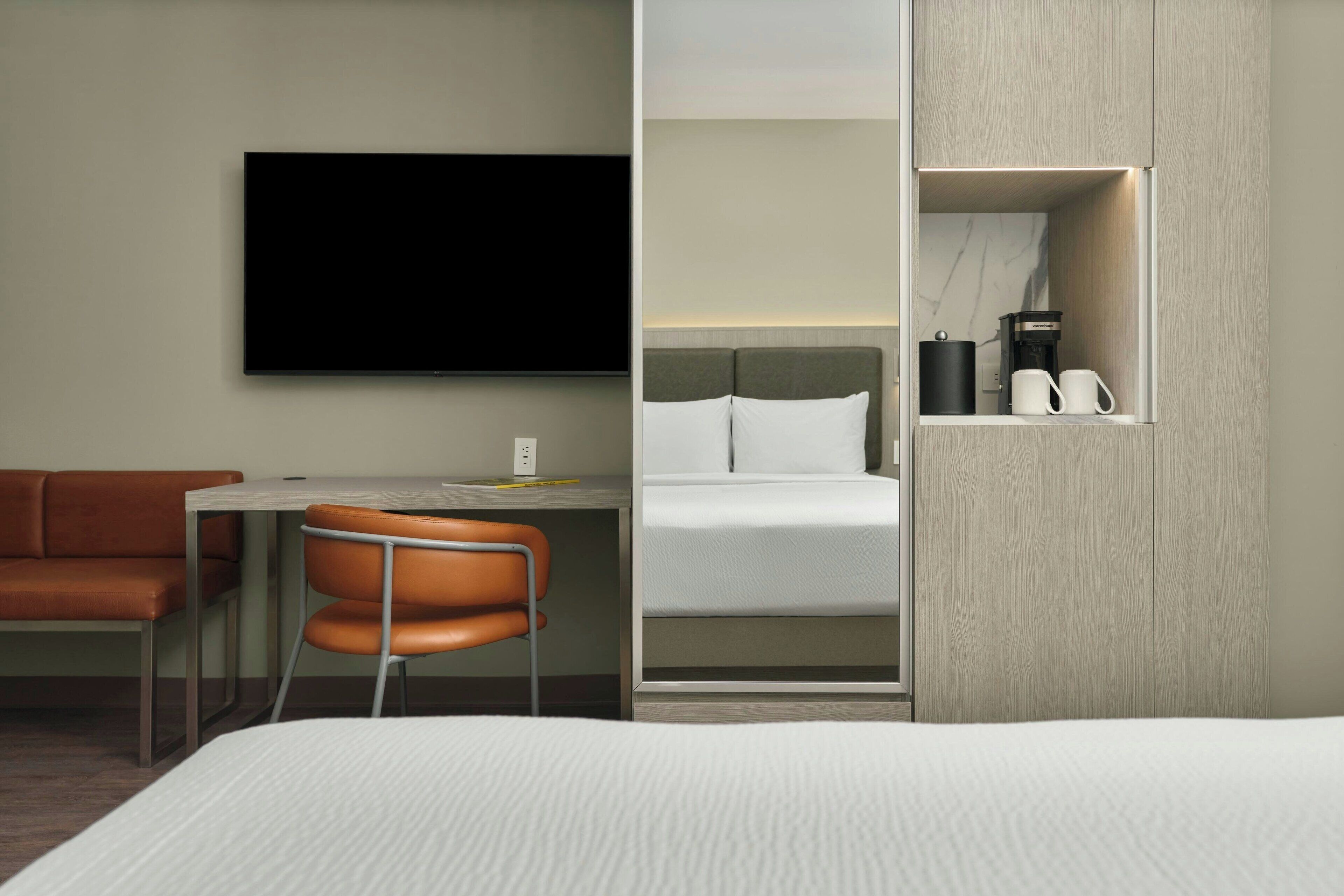 Habitación de hotel con cama, escritorio, silla, televisor y armario con cafetera.