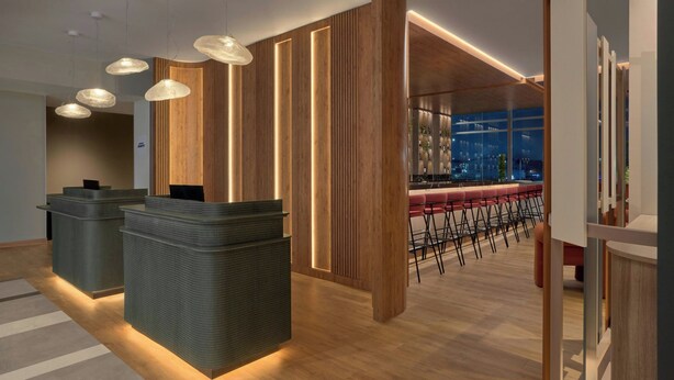 Una moderna zona de recepción con bar y área de descanso, con detalles de madera e iluminación contemporánea.