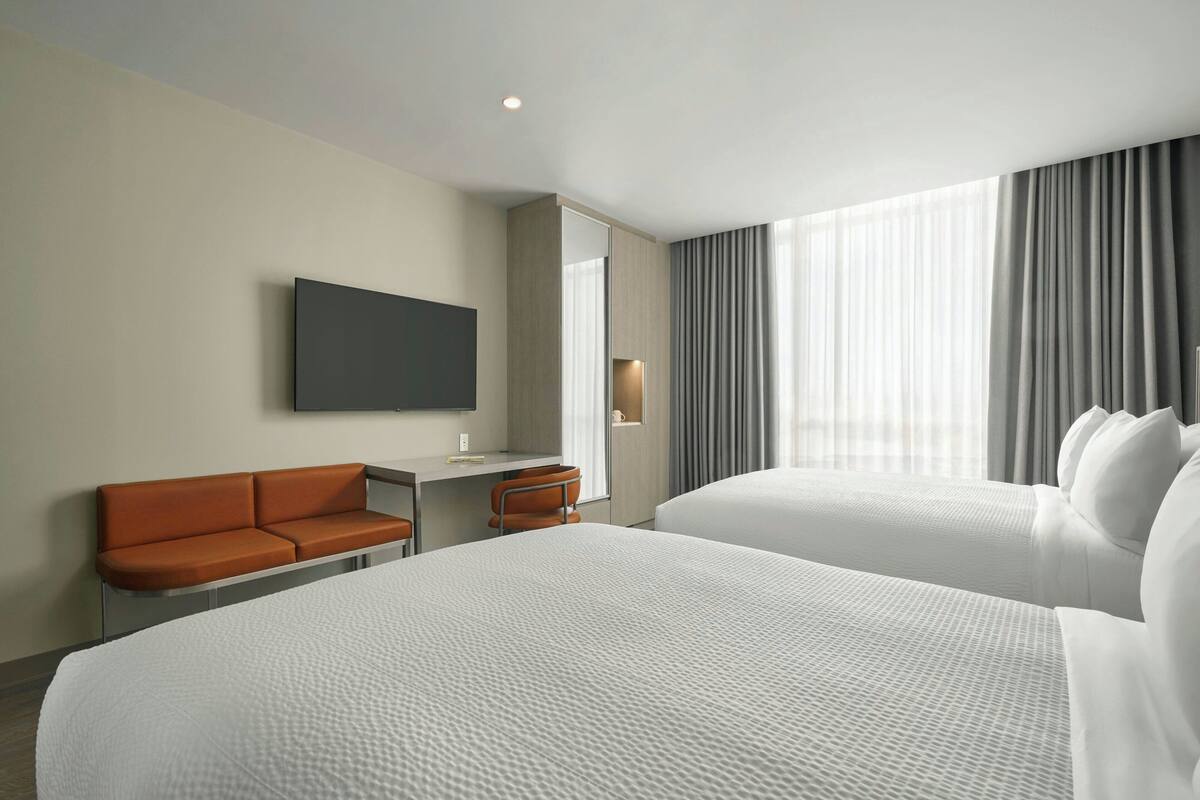 Habitación de hotel con dos camas, un escritorio, una silla y un televisor montado en la pared.