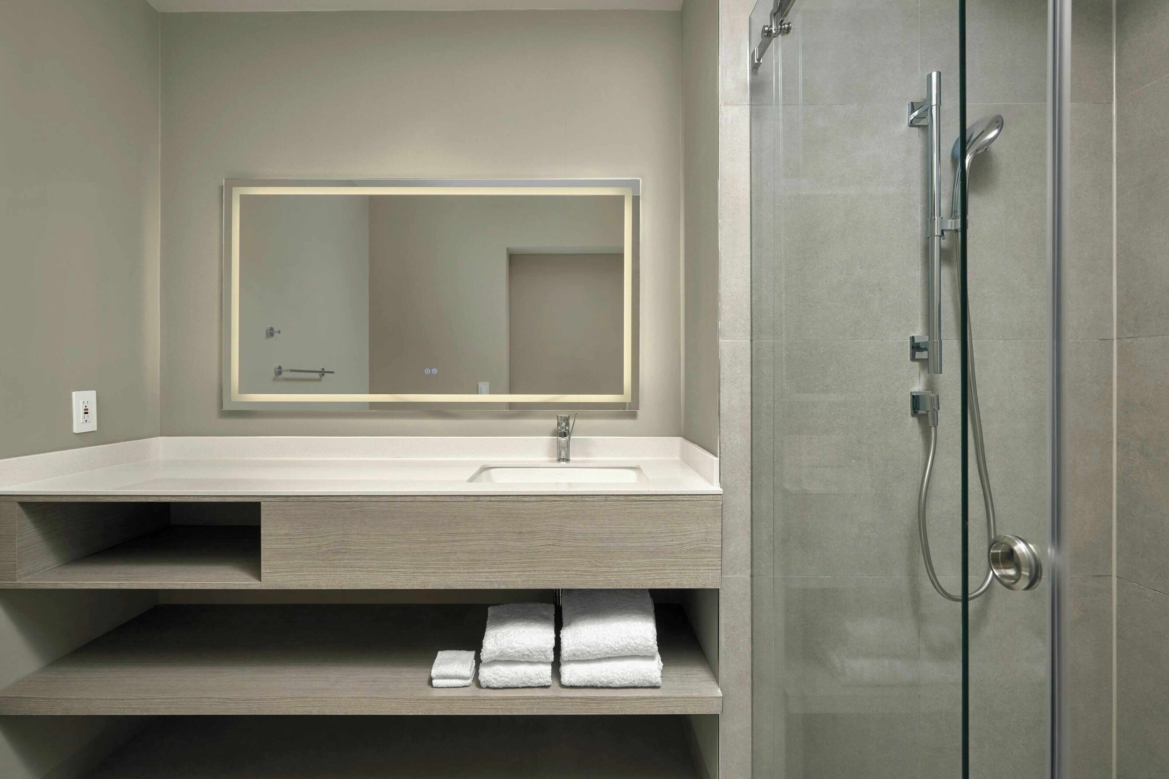 A modern bathroom with a large mirror, a sink, and a shower.