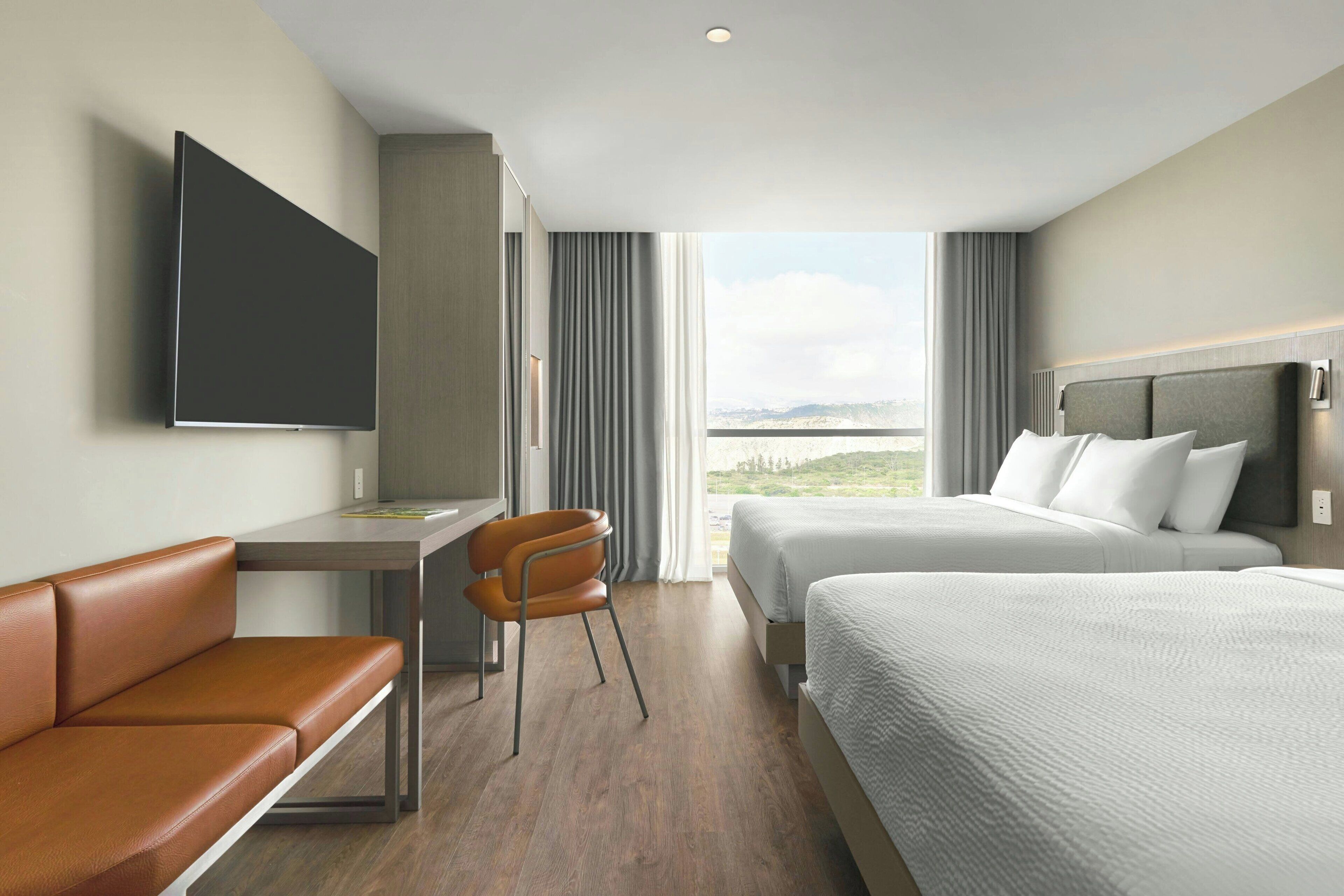 A hotel room with a desk, two beds, a TV, and a view of the outdoors.