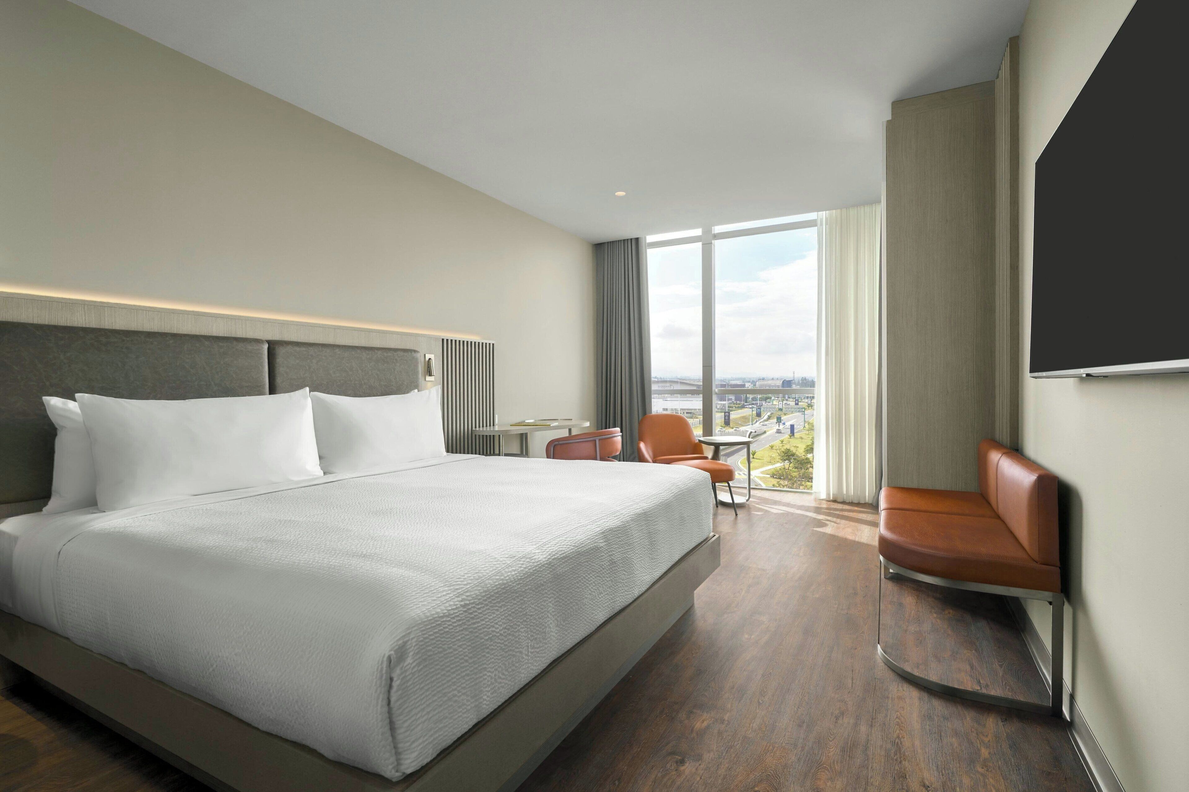 Une chambre d’hôtel moderne, dotée d’un grand lit, d’un bureau, d’une chaise et offrant une vue sur la ville.