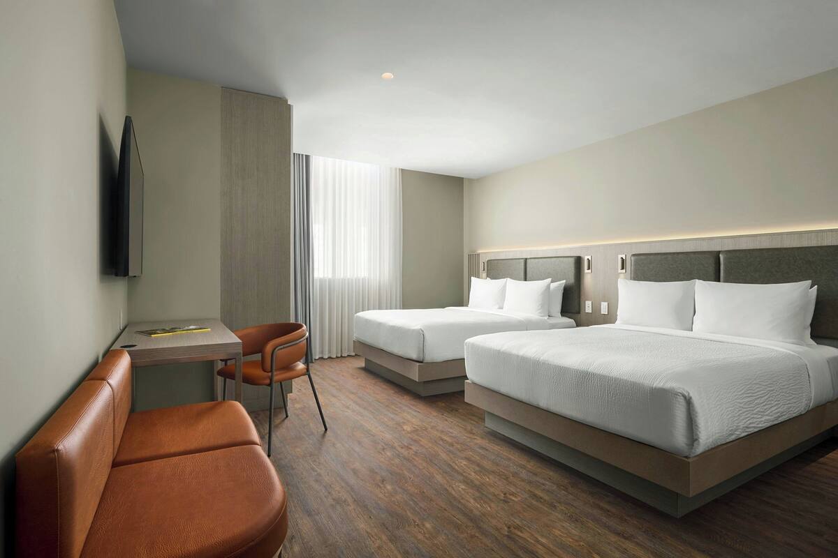 Habitación de hotel con dos camas, un escritorio, una silla y un televisor montado en la pared.