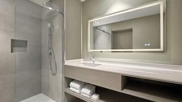 A modern bathroom with a glass-enclosed shower, a sink with a mirror above it, and neatly folded towels on a shelf.