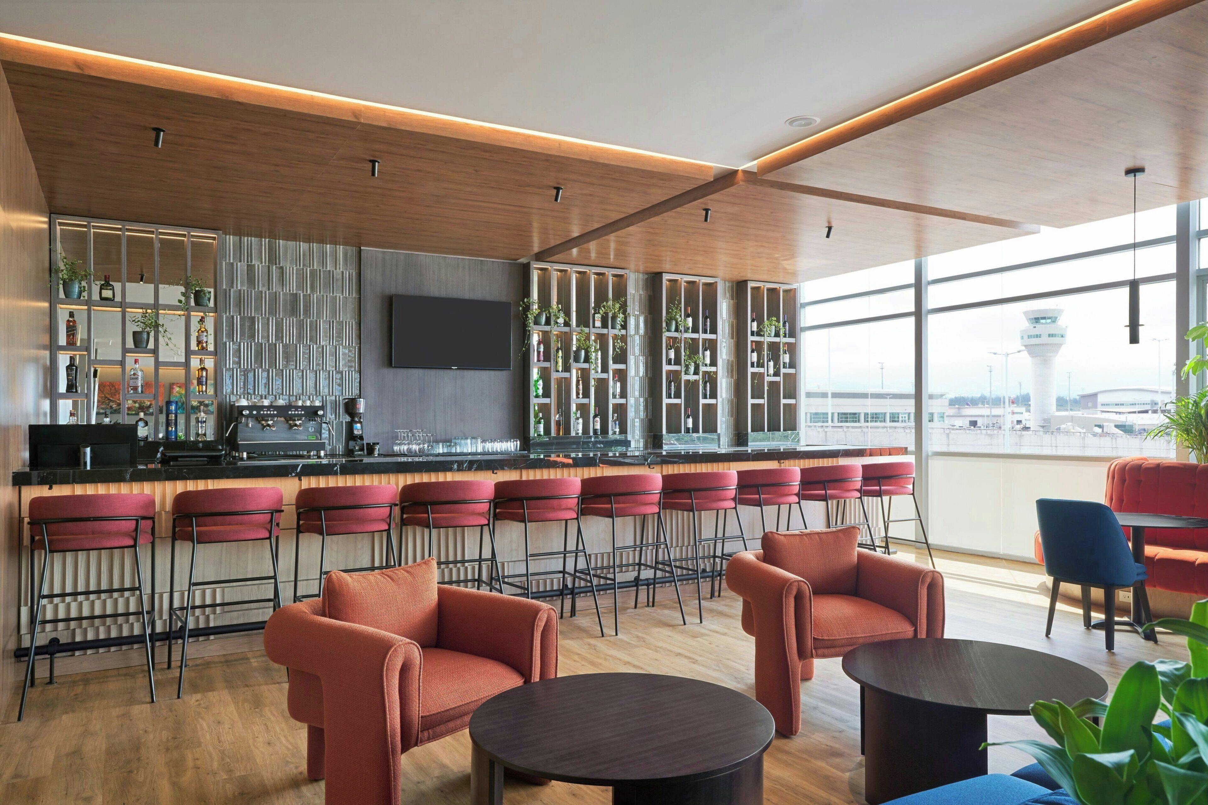 Un bar moderno con taburetes altos, un televisor de pantalla plana y vista al aeropuerto.