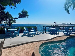 A poolside area with lounge chairs and tables, a clear view of the water, and a flag.