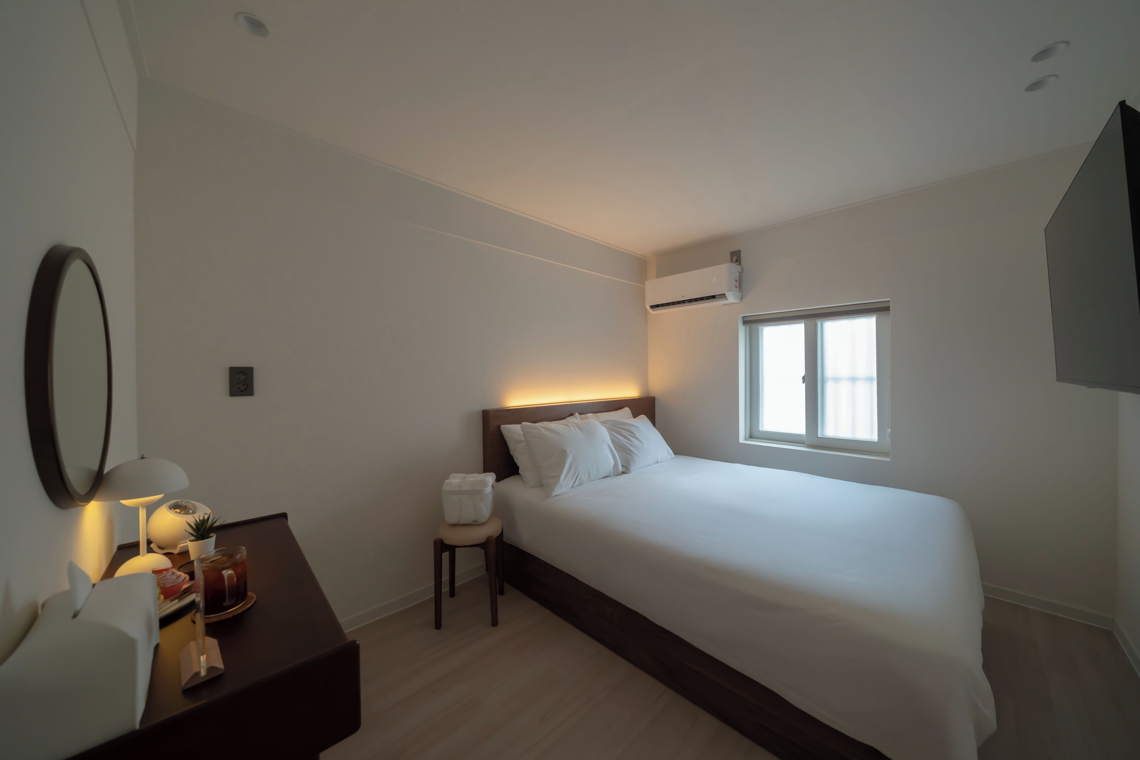 Ein modernes Schlafzimmer mit einem großen Bett, Nachttisch, Lampe und einem kleinen Hocker.