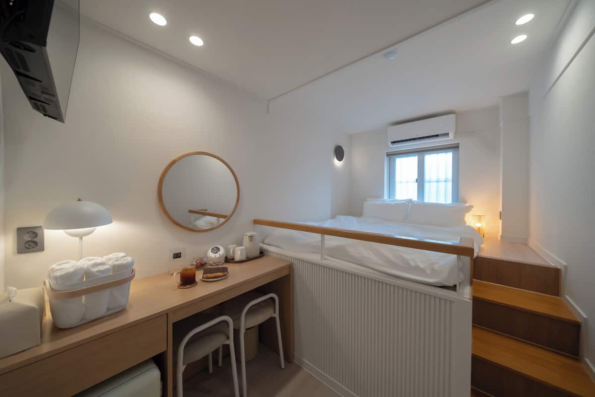 Une chambre d’hôtel moderne équipée d’un lit, d’un bureau, d’une chaise, d’un miroir et d’une fenêtre.