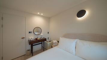 Habitación de hotel con cama, escritorio con espejo, una mesita con tetera y un cubo de basura.