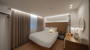 Een moderne hotelkamer met een groot bed, nachtkastje met een lamp, een spiegel en een klein bijzettafeltje met een beker en een boek.