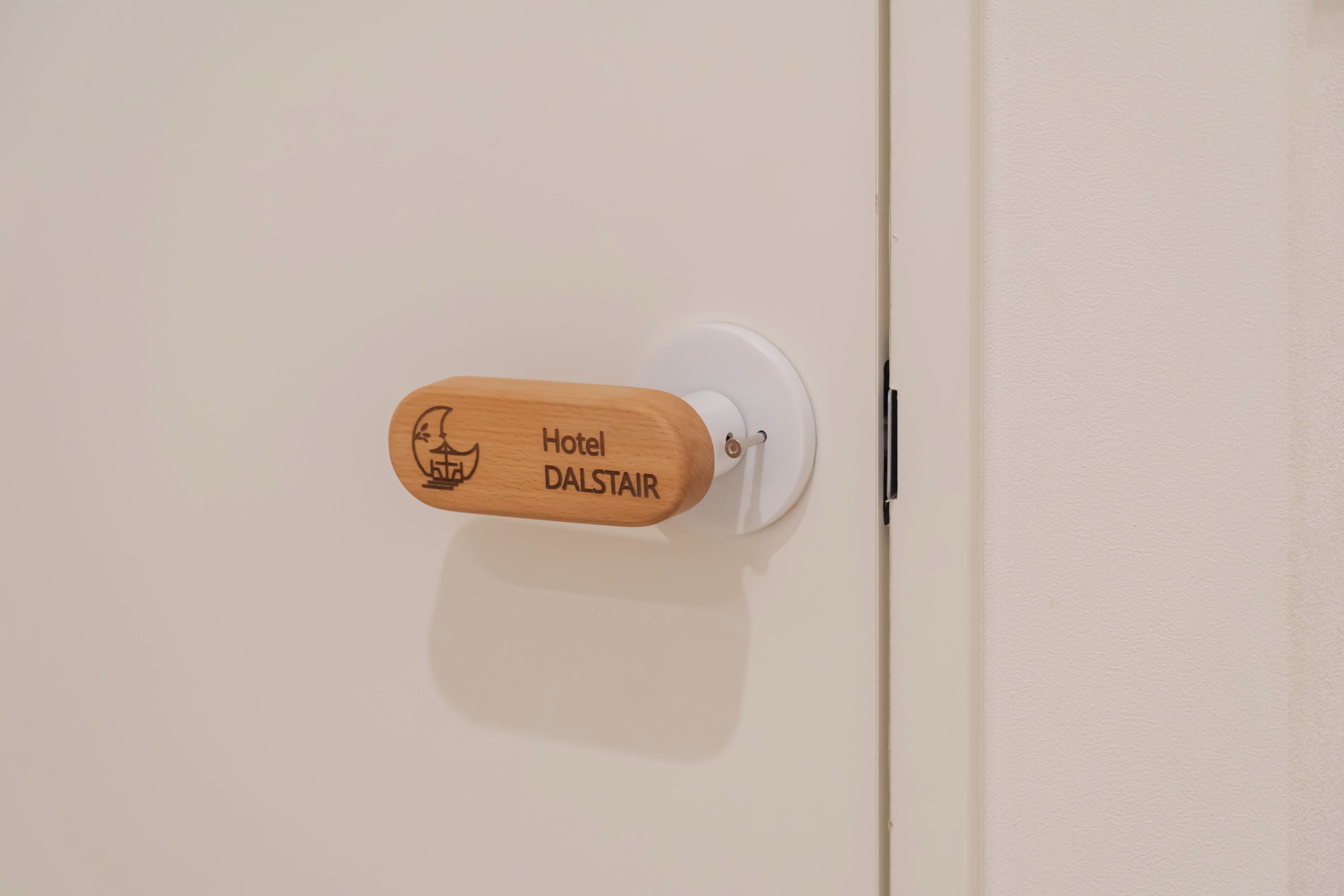 Une poignée de porte en bois pour hôtel, portant l’inscription « Hôtel DALSTAIR » et un logo.