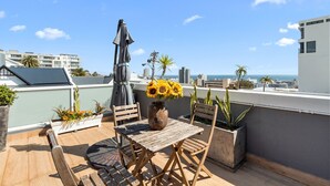 A rooftop terrace with a wooden table and chairs, a vase of sunflowers, and potted plants. - Selbourne Five - Two Bedroom Apartment, Sleeps 4 (Cape Town)