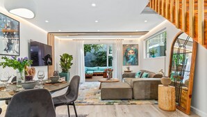 A modern living room with a dining area, a staircase, and a large window. - Selbourne Five - Two Bedroom Apartment, Sleeps 4 (Cape Town)