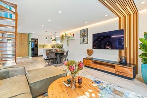 A modern living room with a TV, sofa, coffee table, and a dining area in the background.