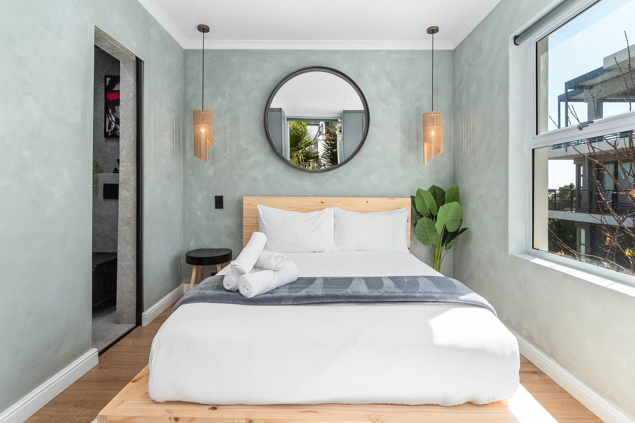 Ein modernes Schlafzimmer mit einem großen Bett, einem runden Spiegel und Blick ins Freie.