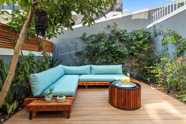 A wooden deck with a blue sofa, a round wooden table, and various plants.
