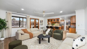 A spacious living room with a large window, a ceiling fan, and a kitchen in the background. - Lakeside Retreat Hot Tub, Fire Pit, 4BR/3BA (Victorville)