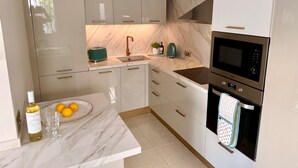 A modern kitchen with white cabinets, a marble backsplash, a built-in oven, and a sink with a gold faucet. - Charming Apartment in Burriana With Private Pool! (Nerja)